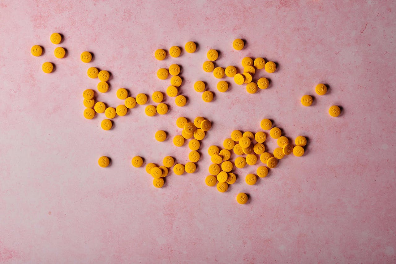 Flat lay of yellow pills scattered on a pink surface, ideal for healthcare themes.