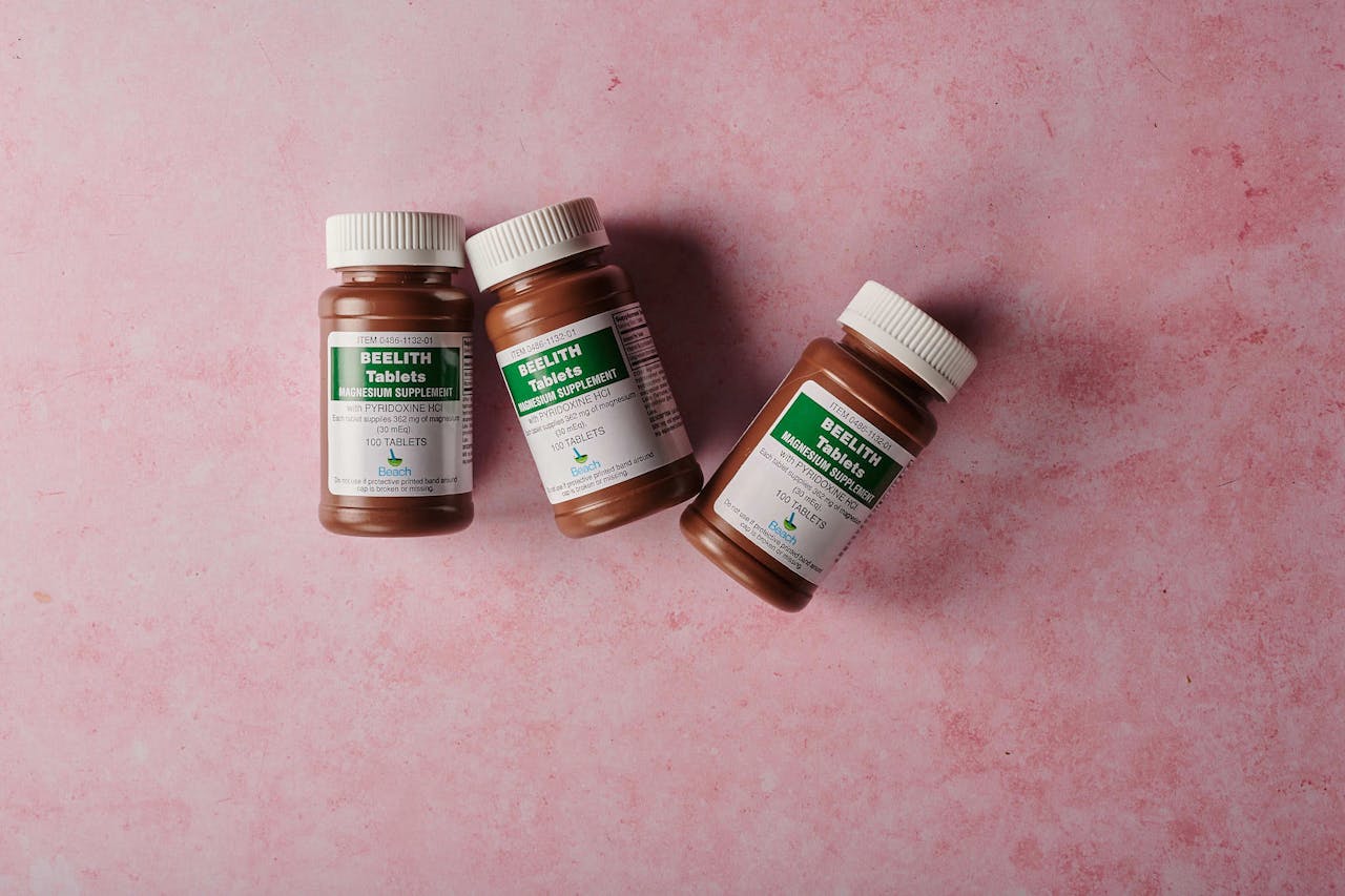 Three brown bottles of magnesium tablets on a soft pink background, ideal for health-themed content.